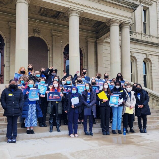 Survivors and youth activists stand on the steps of the Michigan Capital with protest signs.