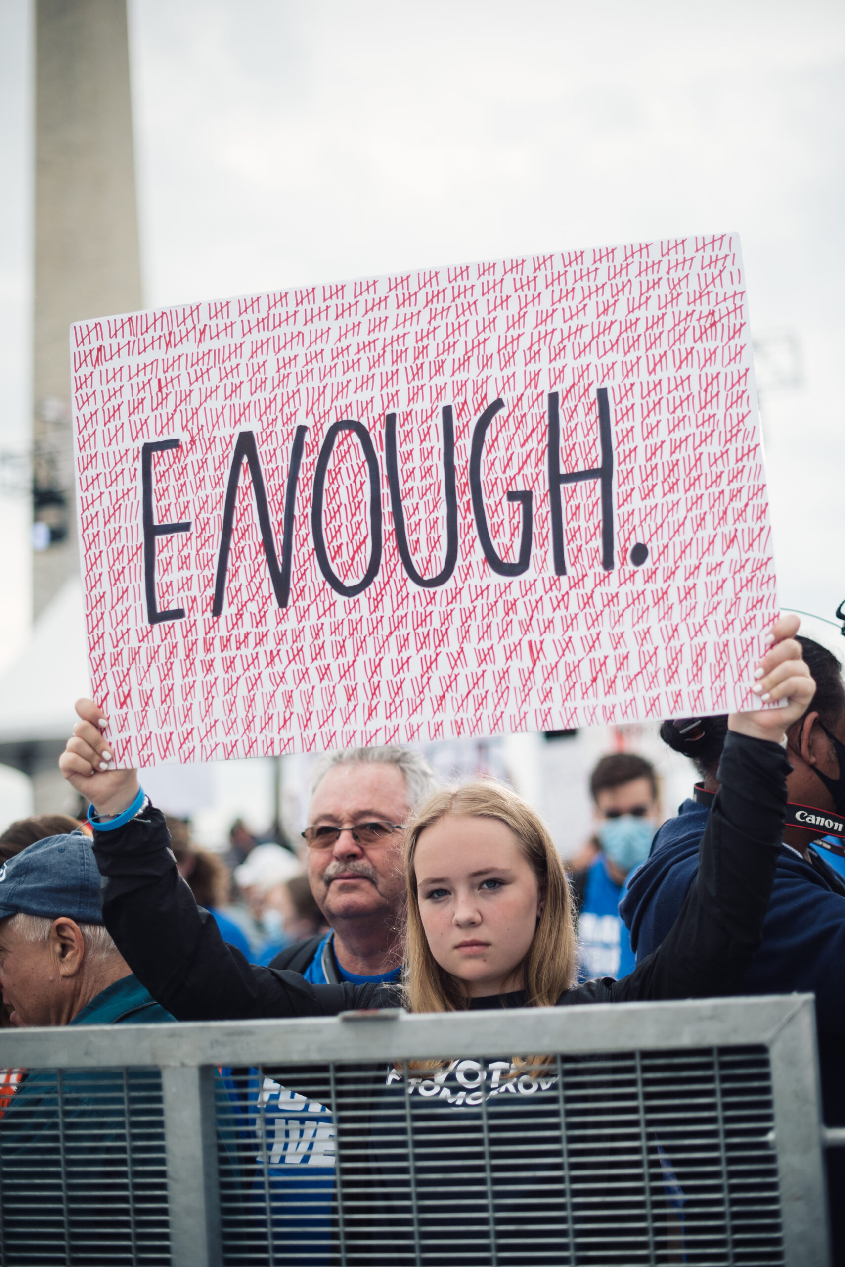 Youth activist holds protest sign reading, "Enough," with hundreds of tally marks to represent lives lost to gun violence.